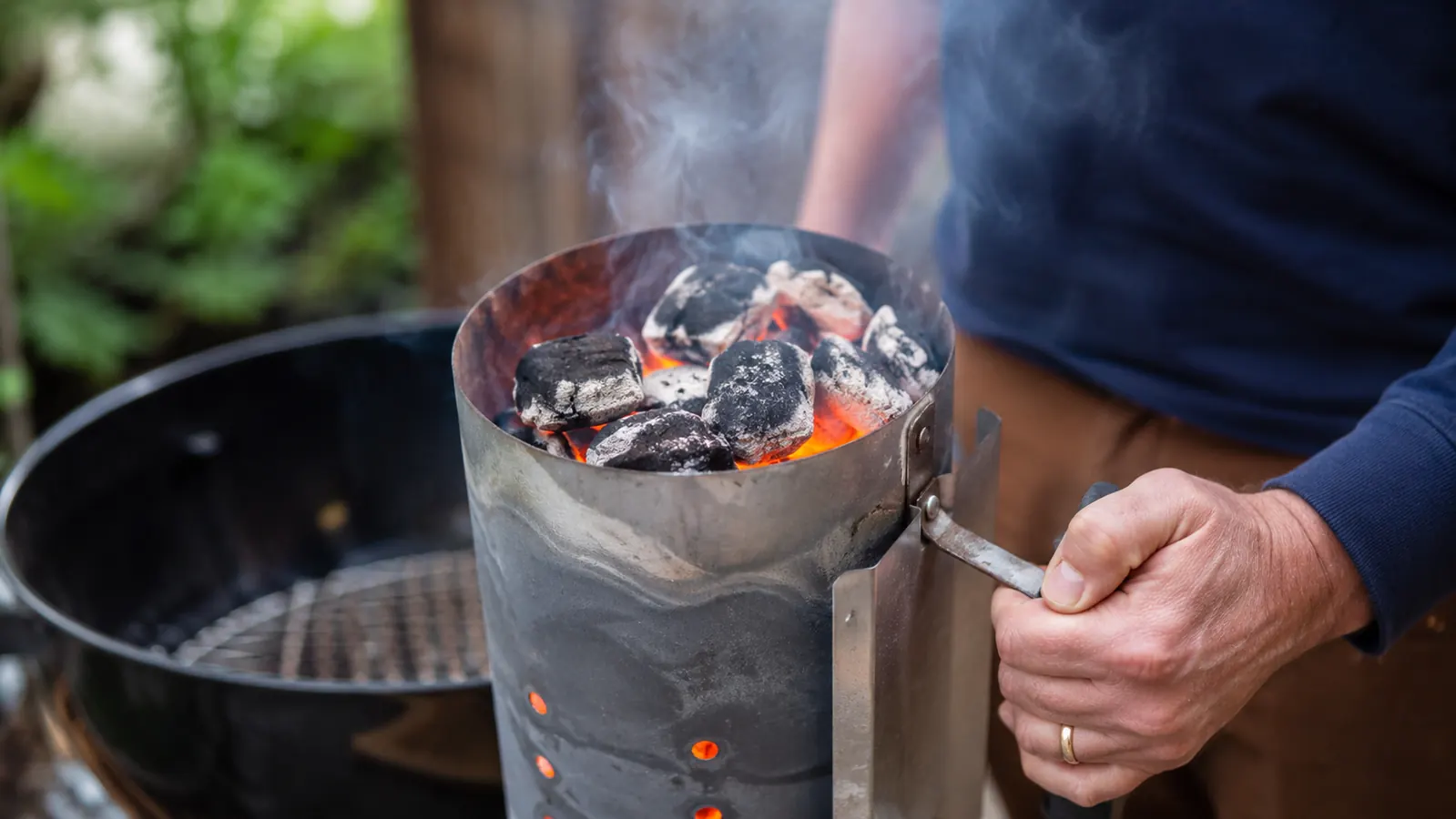 Weber Rapidfire chimney starter glowing orange with fully lit charcoal on a backyard grill deck at dusk
