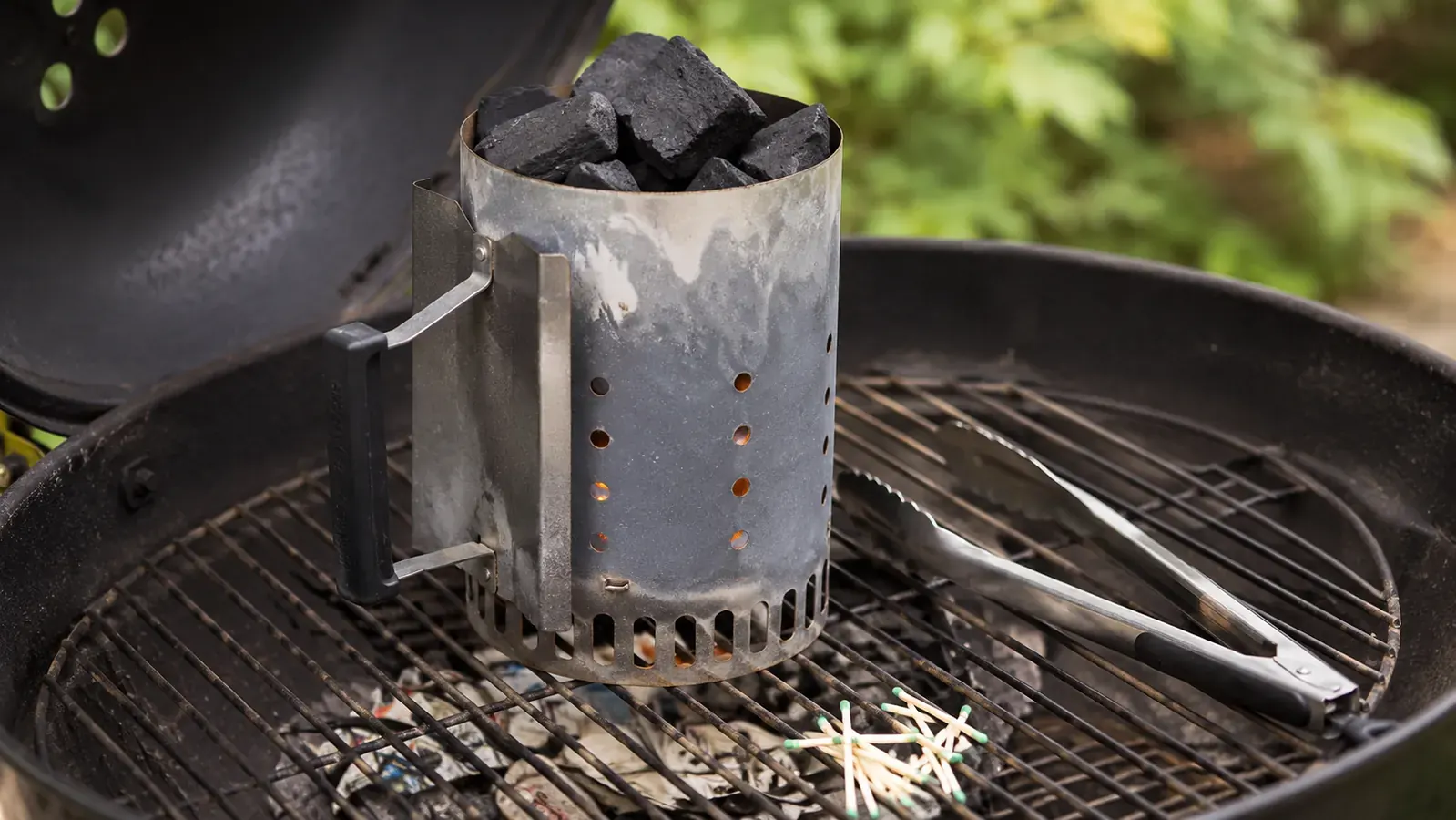 Weber chimney starter with glowing charcoal on a backyard grill, smoke rising in late afternoon light