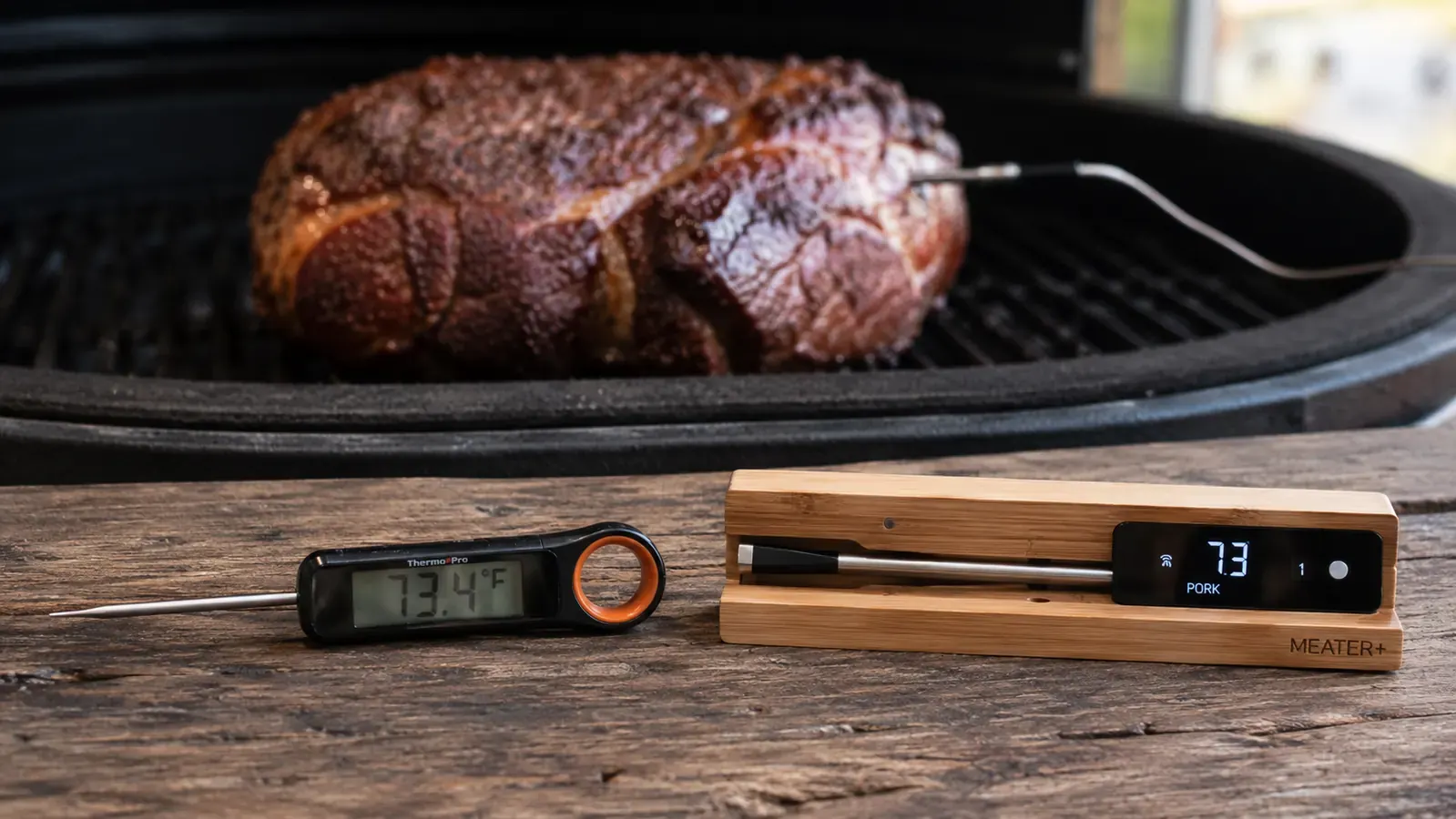 ThermoPro TP19H instant-read thermometer next to a wireless MEATER probe on a wooden cutting board beside a resting steak