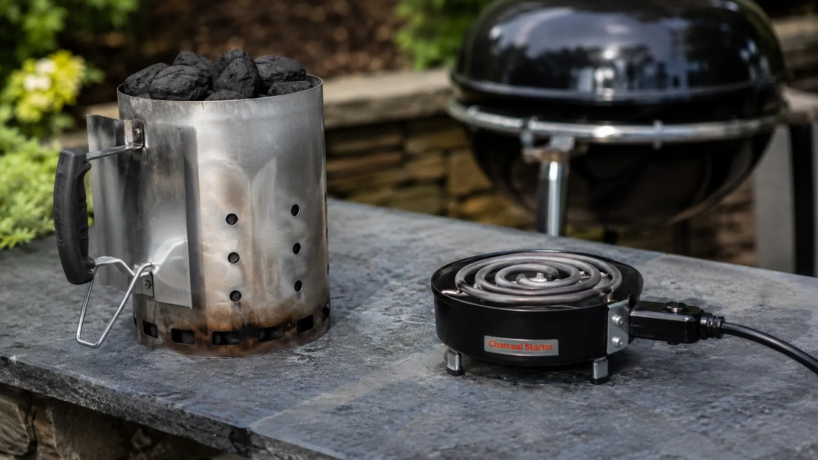 Weber Rapidfire chimney starter loaded with lit charcoal on a backyard patio, glowing coals visible at the top
